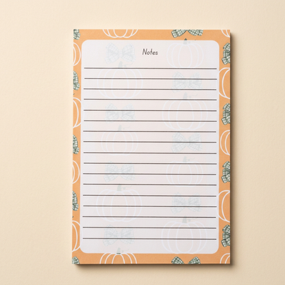 Second pumpkins and green bows notepad on a soft cream background